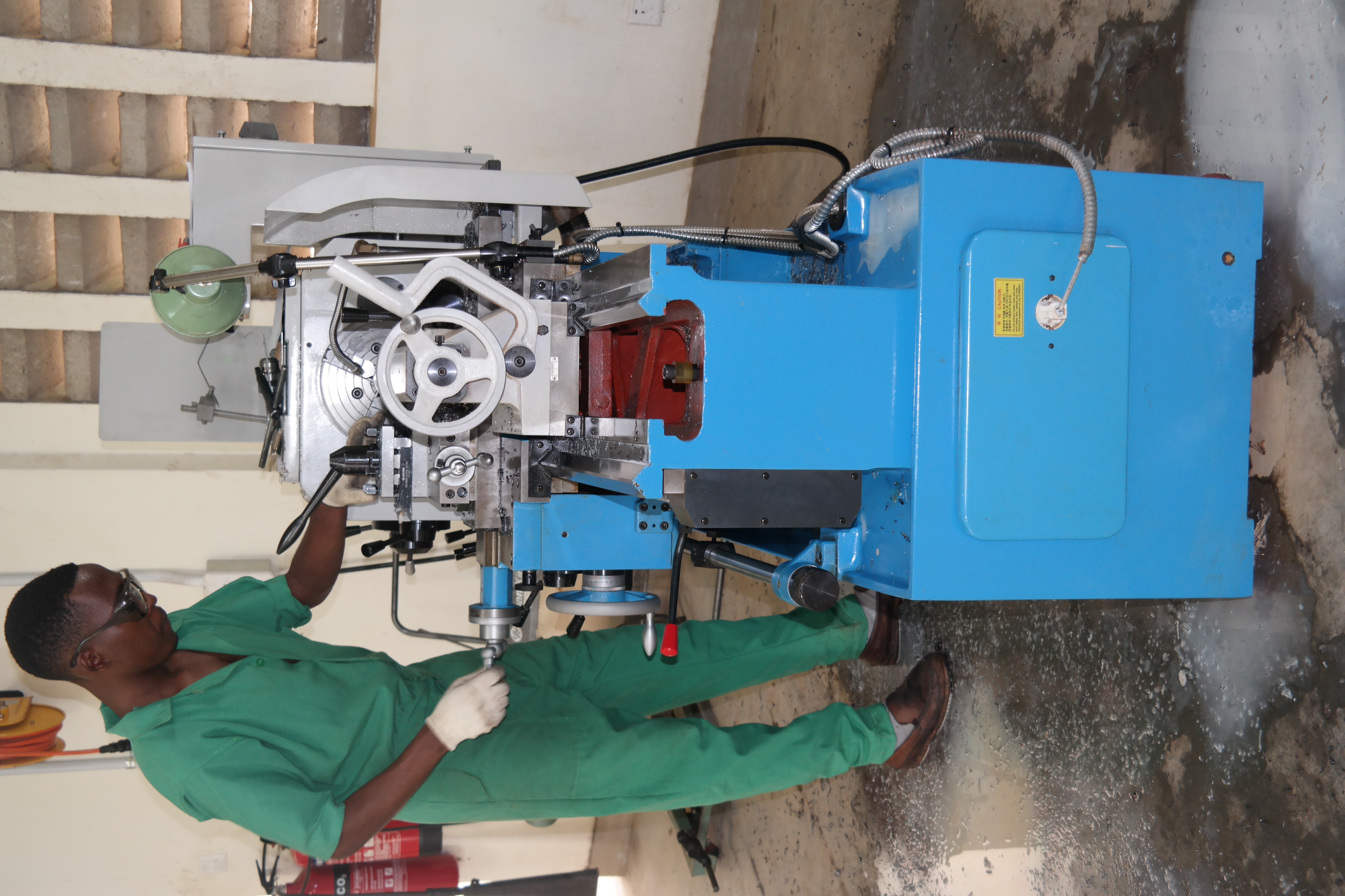 Student operating a lathe machine in green overalls