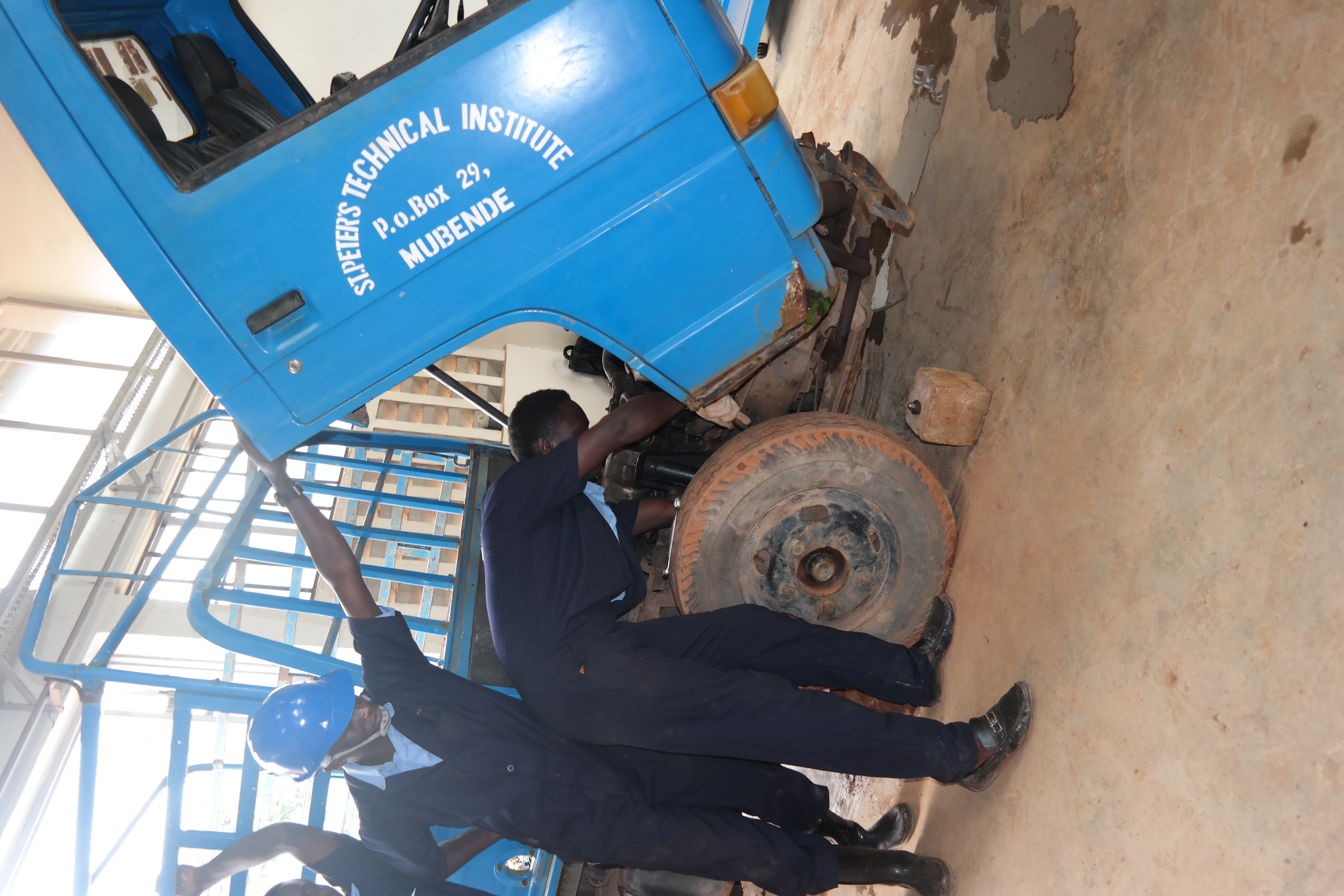 Students working on a blue truck at St. Peter's Technical Institute Mubende
